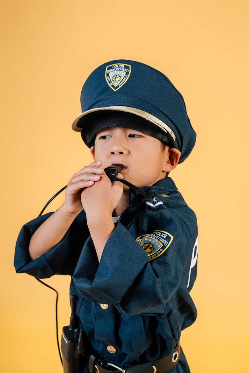 concentrated asian kid in policeman costume blowing whistle